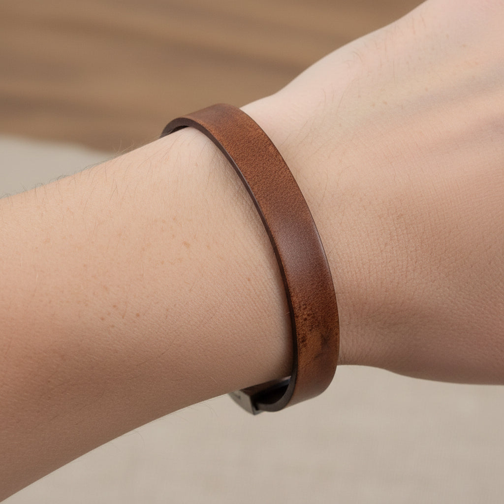 Brown leather bracelet with silver clasp on a wrist against a beige background