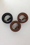 Three leather watch straps in dark brown, medium brown, and black, each with silver-toned metal buckles, laid out vertically on a light textured background.