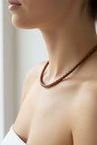Women wearing a brown braided necklace against a neutral backgroundan