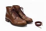 A pair of burgundy round leather shoelaces with metal aglet tips.